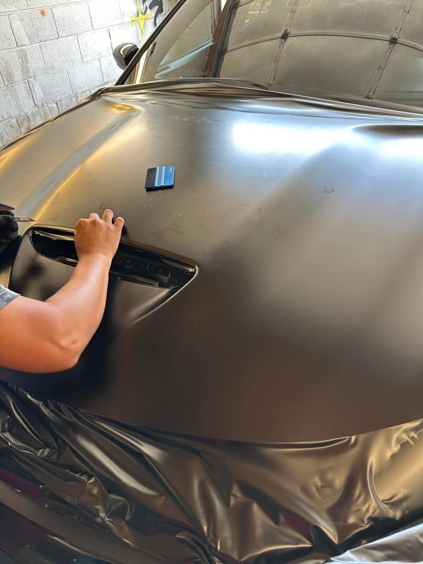 Satin black hood wrap install squeegee finish